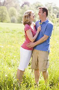 Couple embracing outdoors holding flower smiling