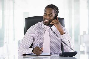 Businessman sitting in office with personal organizer open on telephone