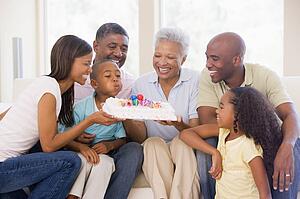 Family in living room smiling with young boy blowing out candles on cake