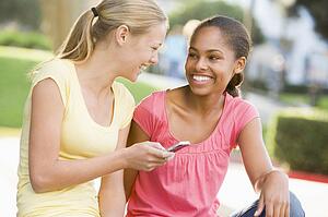 Teenage Girls Sitting Outside Playing With Mobile Phone