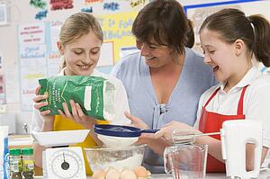 Students preparing ingredients in cooking class with teacher