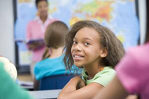 Student in class looking at camera with teacher in background (selective focus)