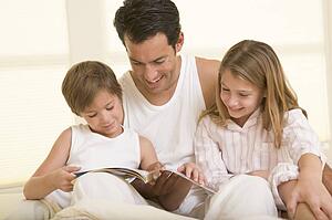 Man with two young children sitting in bed reading a book and smiling