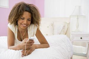 Teenage Girl Lying On Bed Using Mp3 Player