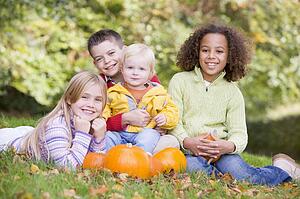 Three young friends with baby sitting on grass with pumpkins smiling