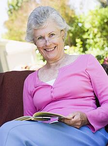 Senior woman sitting outdoors on a chair reading a book