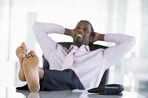 Businessman sitting in office with feet on desk relaxing and smiling
