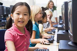 Children at computer terminals with teacher in background (depth of field/high key)