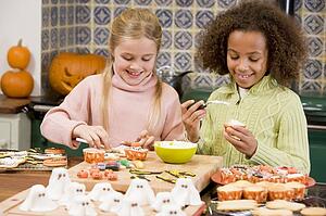 Two young girl friends at Halloween making treats and smiling