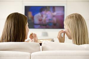 Two women in living room watching television eating chocolates and crying