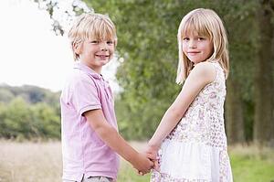Two young children standing outdoors holding hands smiling