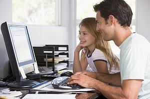 Man and young girl in home office with computer smiling