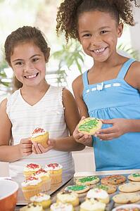 Two children in kitchen decorating cookies smiling