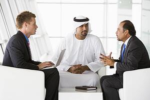 Three businessmen indoors with a laptop talking and smiling (high key/selective focus)