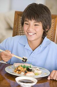 Young boy in dining room eating chinese food smiling