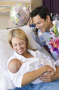 New mother with baby and husband in hospital smiling