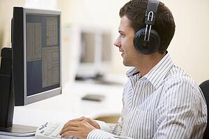 Man wearing headphones in computer room typing and smiling