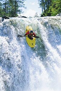 Kayaker in rapids coming over waterfall (selective focus)