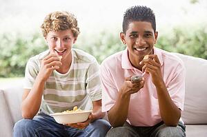 Teenage Boys Sitting On Couch Eating crisps Together