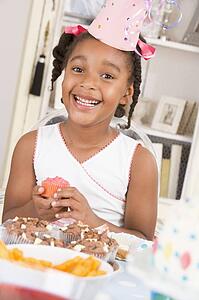 Young girl at party sitting at table with a cupcake smiling