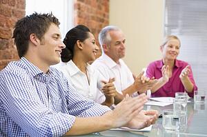 Four businesspeople in boardroom applauding and smiling