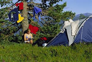 Woman outdoors at campsite reading book by hanging clothes