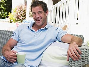 Man sitting on patio with coffee laughing