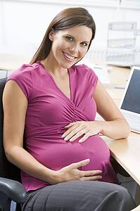 Pregnant woman at work holding belly and smiling