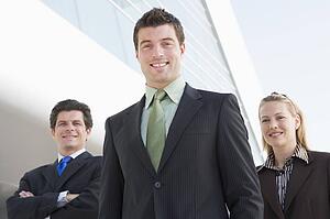 Three businesspeople standing outdoors by building smiling