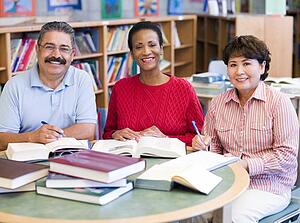 Three people sitting in library with books and notepads (selective focus)