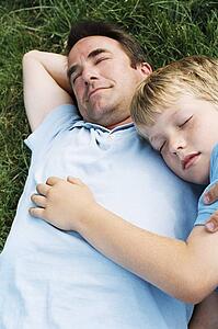 Father and son lying outdoors sleeping