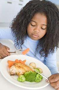Young girl in kitchen eating chicken and vegetables