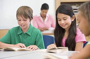 Students in class reading with teacher in background (selective focus)