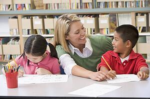 Two students in class writing with teacher helping
