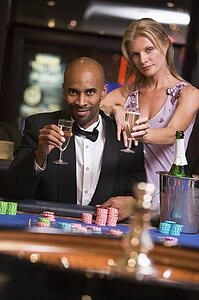 Couple in casino at roulette table holding champagne and smiling (selective focus)