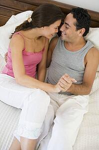 Couple relaxing on bed holding hands in bedroom smiling (selective focus)