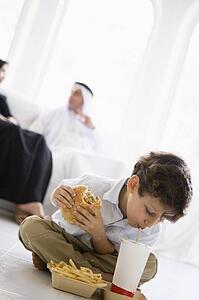 Young boy with fast food in living room with parents in background (high key/selective focus)