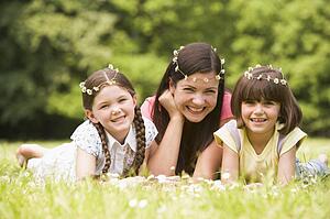 Mother and daughters lying outdoors with flowers smiling