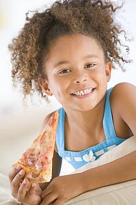 Young girl eating pizza slice in living room smiling