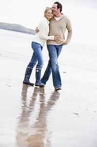 Couple walking on beach arm in arm smiling