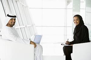 Two businesspeople indoors with a laptop smiling (high key/selective focus)