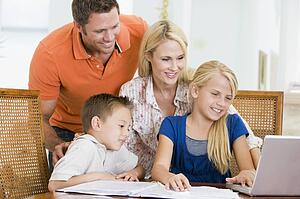 Couple helping two young children with laptop do homework in dining room