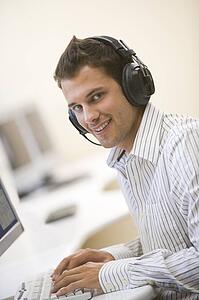 Man wearing headphones in computer room typing and smiling
