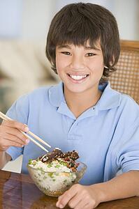 Young boy in dining room eating chinese food smiling