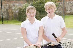 Two young friends with rackets on tennis court smiling