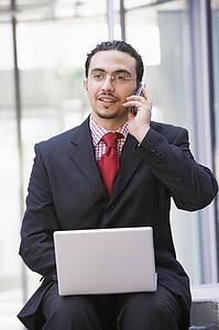 Businessman sitting outdoors by building with a laptop on cellular phone (high key/selective focus)