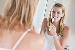 Woman in bathroom brushing teeth smiling