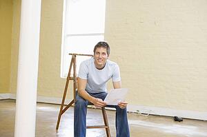 Man sitting on ladder in empty space holding paper smiling