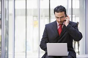 Businessman sitting outdoors by building with a laptop on cellular phone (high key/selective focus)