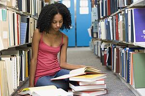 Woman sitting on floor in library reading book